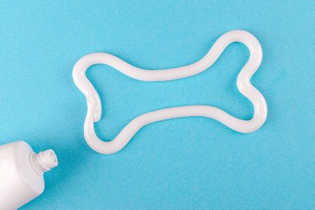 A tube of toothpaste squeezing out toothpaste in the shape of a bone